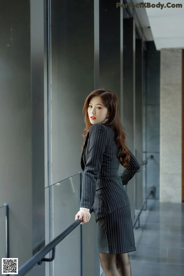 A woman in a business suit leaning against a railing.