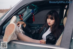 A woman sitting on top of a black car.