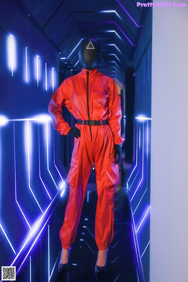 A mannequin wearing a red jumpsuit and a black mask.