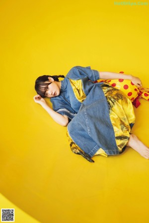 A woman laying on a yellow surface with a yellow background.