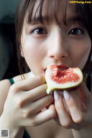 A woman eating a fig in front of her face.