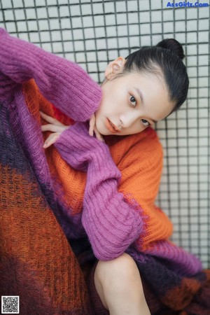 A woman sitting on a wooden bench wearing a colorful sweater.