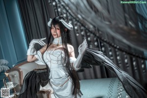 A woman with long black hair wearing a white dress and gloves.