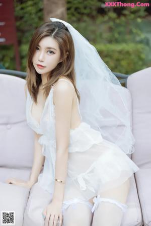 A woman in a wedding dress kneeling on a bench.