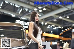 A woman standing next to a brown car on display.