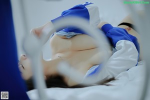 A woman in a blue and white jacket sitting on a bed.