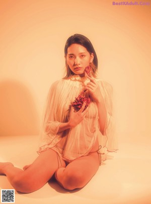 A woman in a red dress sitting on a white cube.