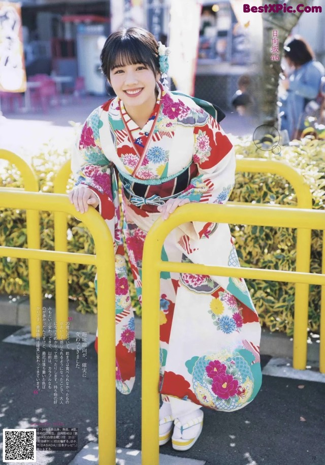 A woman in a kimono leaning against a yellow fence.