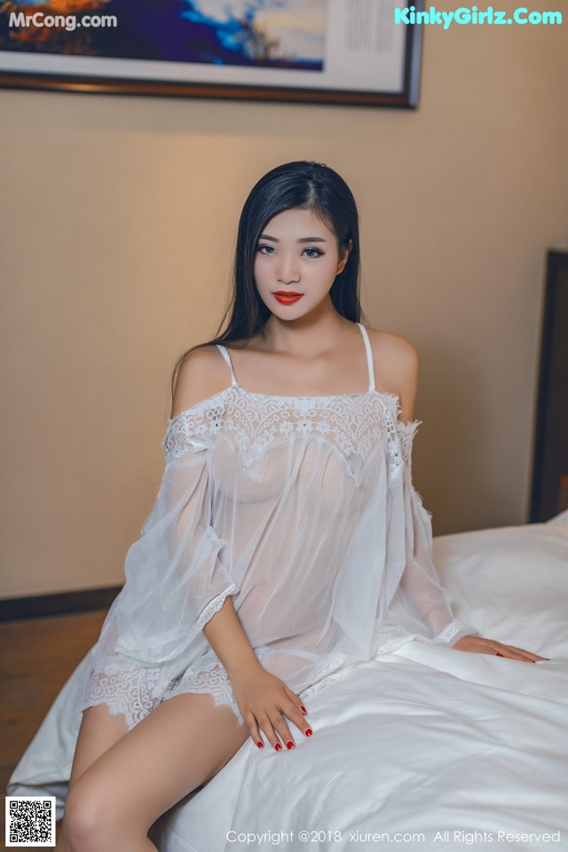 A woman in a white dress sitting on a bed.
