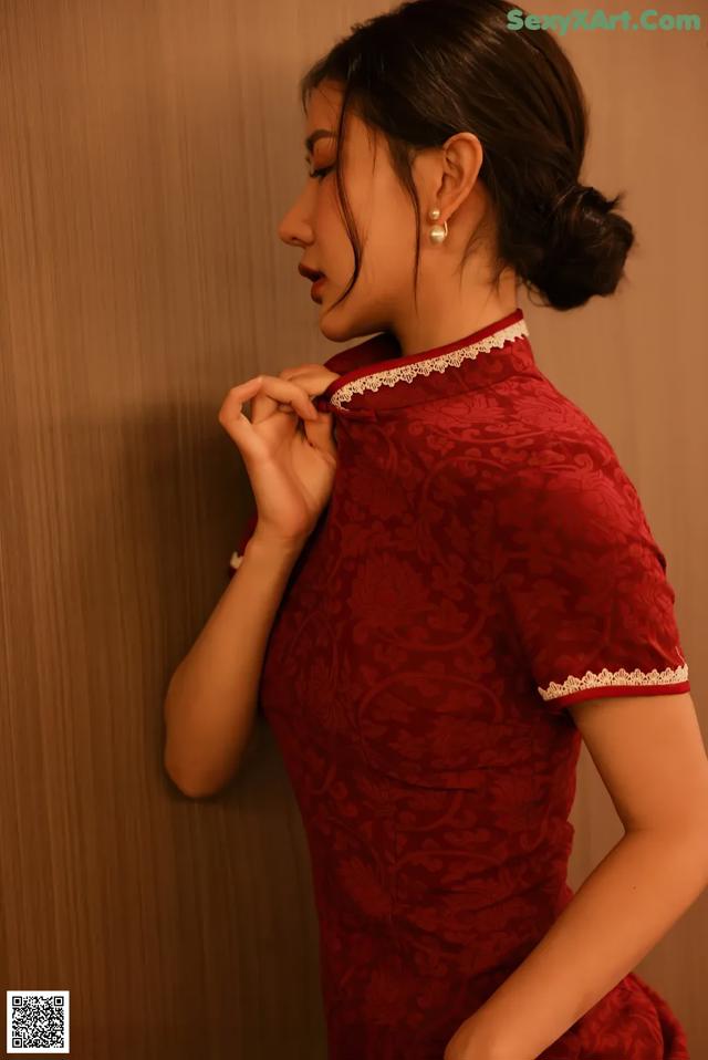 A woman in a red cheongsam leaning against a wall.