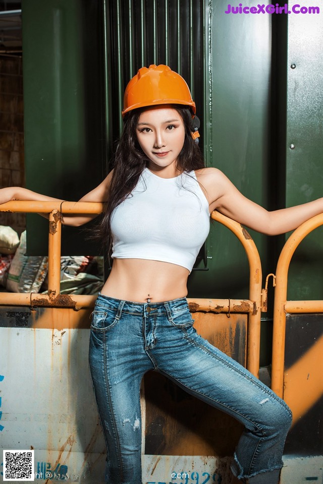 A woman wearing a hard hat leaning against a fence.