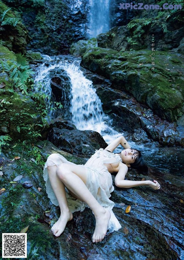 A woman laying on a rock in front of a waterfall.