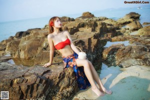 A woman in a red bikini sitting on a blue and white checkered blanket.