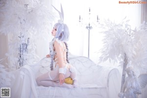 A woman in a white bunny costume sitting on a bed.