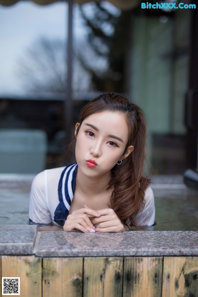 A woman leaning over a wooden bench with her hand on her chin.